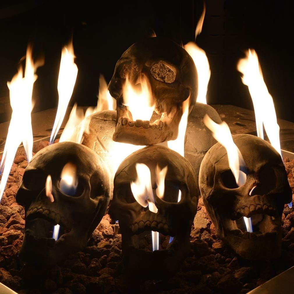 Cement skull-shaped gas log with fiery flames coming from its eyes and mouth, ideal for Halloween fire pits.